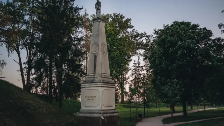 Kamienny pomnik na postumencie w otoczeniu drzew w bydgoskim parku w świetle dziennym.
